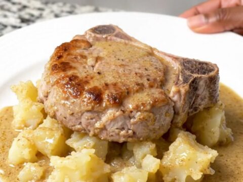 A close-up of tender braised pork chops served alongside creamy scalloped potatoes in a rich mushroom sauce on a white plate.