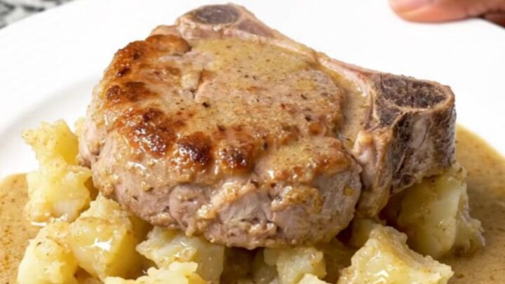 A close-up of tender braised pork chops served alongside creamy scalloped potatoes in a rich mushroom sauce on a white plate.