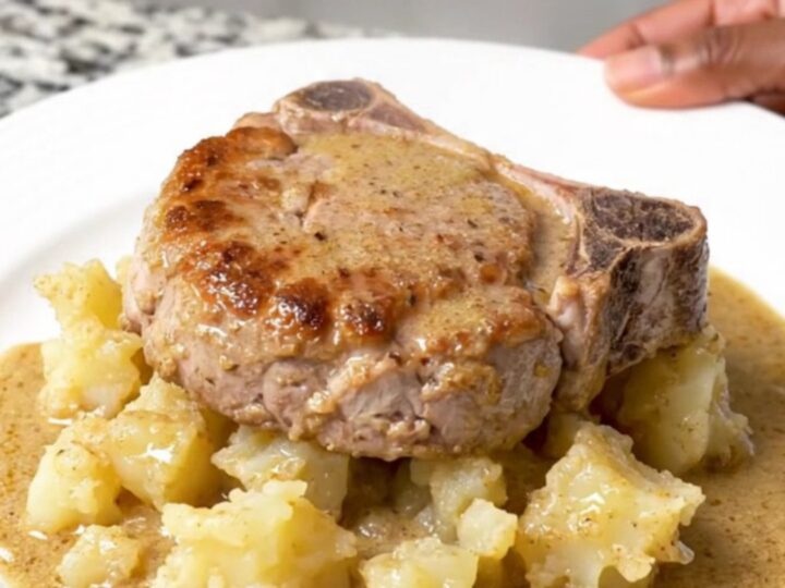 A close-up of tender braised pork chops served alongside creamy scalloped potatoes in a rich mushroom sauce on a white plate.