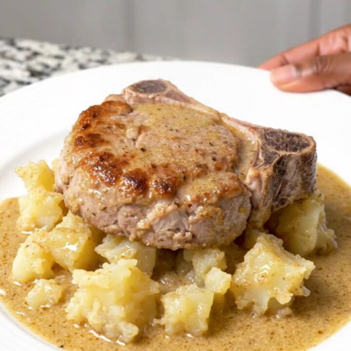 A close-up of tender braised pork chops served alongside creamy scalloped potatoes in a rich mushroom sauce on a white plate.
