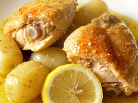 A close-up of slow cooker Greek lemon chicken and potatoes in a stoneware crock, showing tender meat and golden potatoes.
