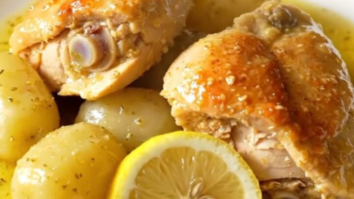 A close-up of slow cooker Greek lemon chicken and potatoes in a stoneware crock, showing tender meat and golden potatoes.