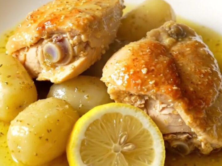 A close-up of slow cooker Greek lemon chicken and potatoes in a stoneware crock, showing tender meat and golden potatoes.