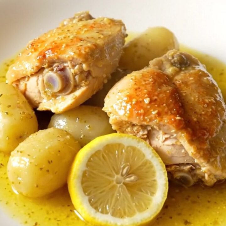 A close-up of slow cooker Greek lemon chicken and potatoes in a stoneware crock, showing tender meat and golden potatoes.