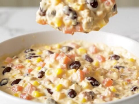 A top-down view of a black slow cooker filled with Cowboy Queso, featuring visible ground beef, beans, corn, and cheese.