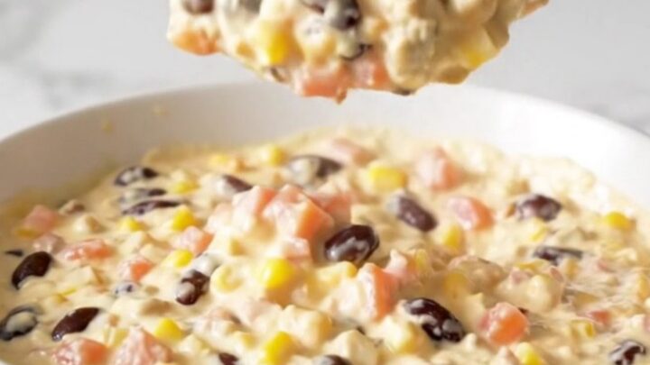 A top-down view of a black slow cooker filled with Cowboy Queso, featuring visible ground beef, beans, corn, and cheese.