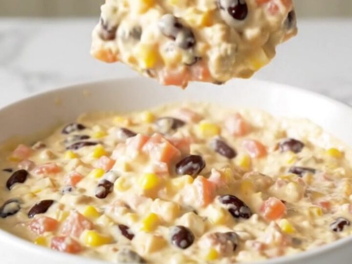 A top-down view of a black slow cooker filled with Cowboy Queso, featuring visible ground beef, beans, corn, and cheese.