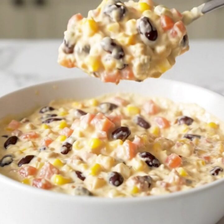 A top-down view of a black slow cooker filled with Cowboy Queso, featuring visible ground beef, beans, corn, and cheese.