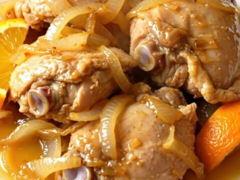 A close-up shot of tender, shredded chicken carnitas served on a white plate with visible citrus juices.