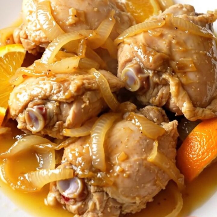 A close-up shot of tender, shredded chicken carnitas served on a white plate with visible citrus juices.