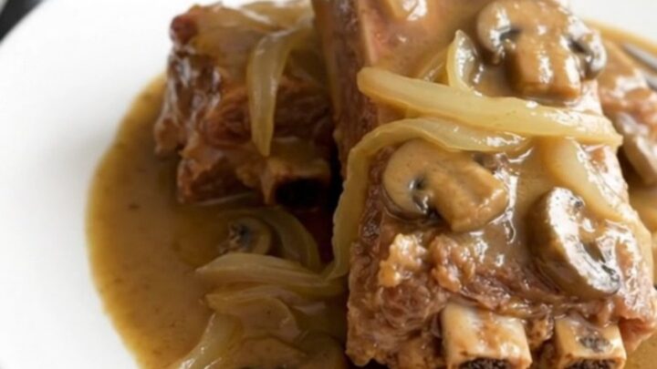 A close-up of tender, bone-in country-style pork ribs smothered in a thick, creamy mushroom gravy with visible onion slices.