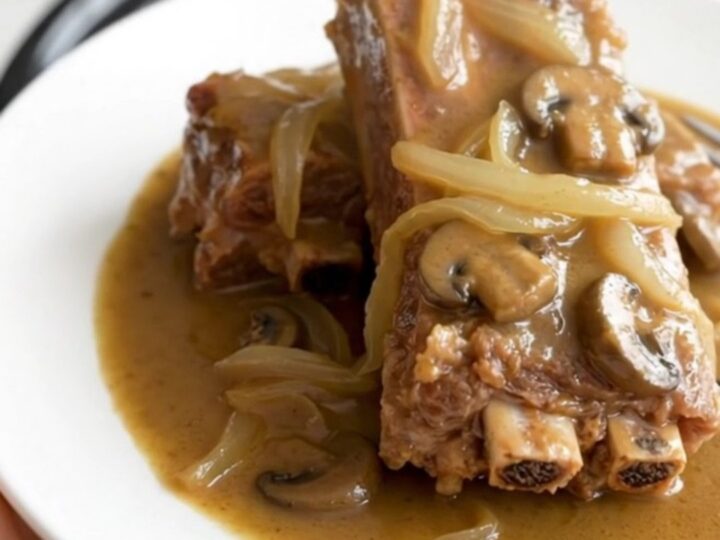 A close-up of tender, bone-in country-style pork ribs smothered in a thick, creamy mushroom gravy with visible onion slices.