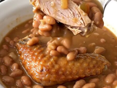 A top-down view of a slow cooker filled with a rich Cajun bean stew featuring smoked turkey wings.