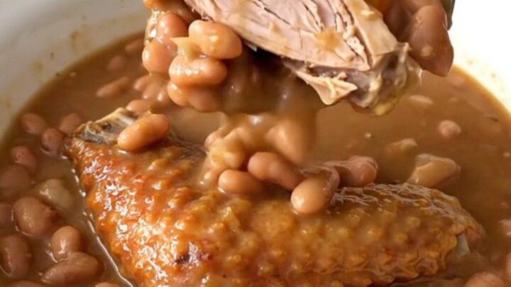 A top-down view of a slow cooker filled with a rich Cajun bean stew featuring smoked turkey wings.