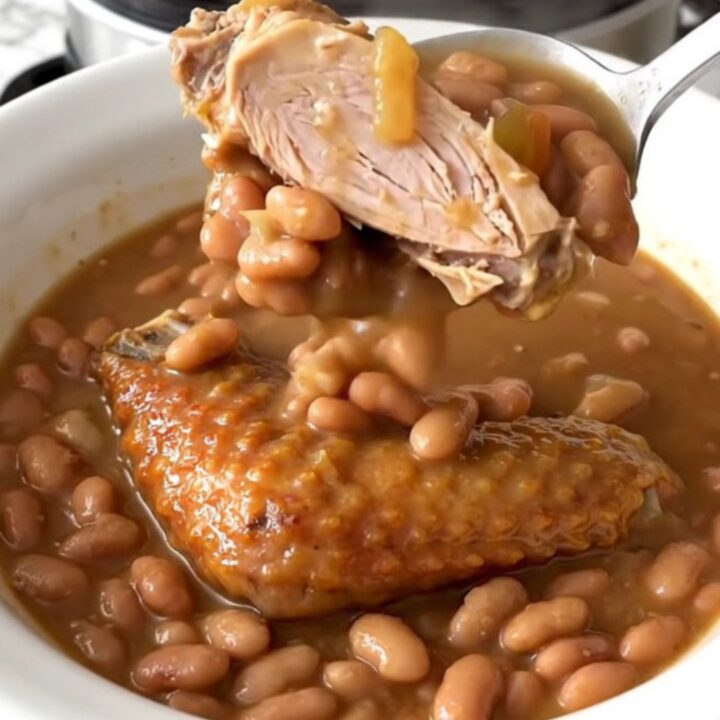 A top-down view of a slow cooker filled with a rich Cajun bean stew featuring smoked turkey wings.