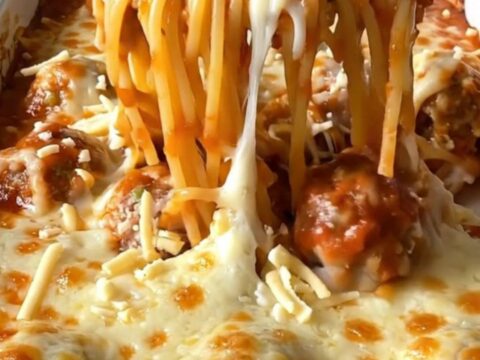 A top-down view of a rectangular baking dish filled with spaghetti, meatballs, and melted mozzarella cheese.