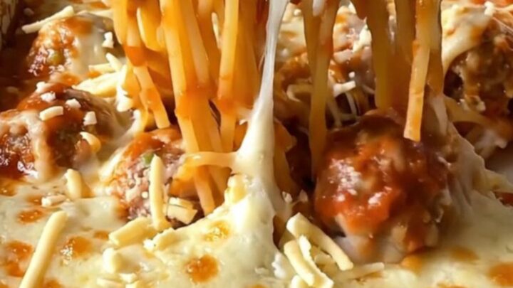 A top-down view of a rectangular baking dish filled with spaghetti, meatballs, and melted mozzarella cheese.