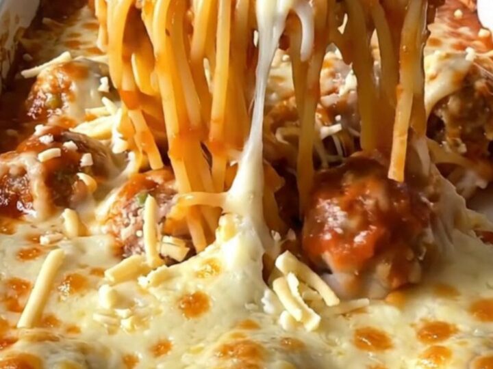 A top-down view of a rectangular baking dish filled with spaghetti, meatballs, and melted mozzarella cheese.