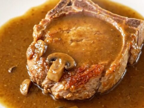A close-up of tender, bone-in pork chops covered in a rich, creamy mushroom and onion gravy in a slow cooker.