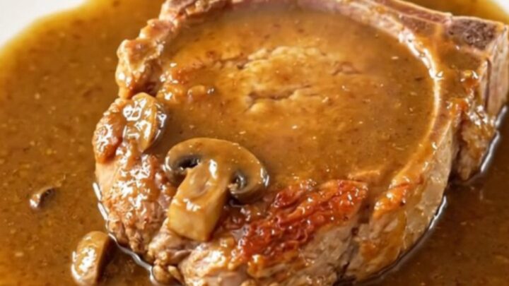 A close-up of tender, bone-in pork chops covered in a rich, creamy mushroom and onion gravy in a slow cooker.