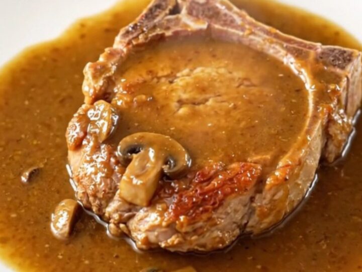 A close-up of tender, bone-in pork chops covered in a rich, creamy mushroom and onion gravy in a slow cooker.