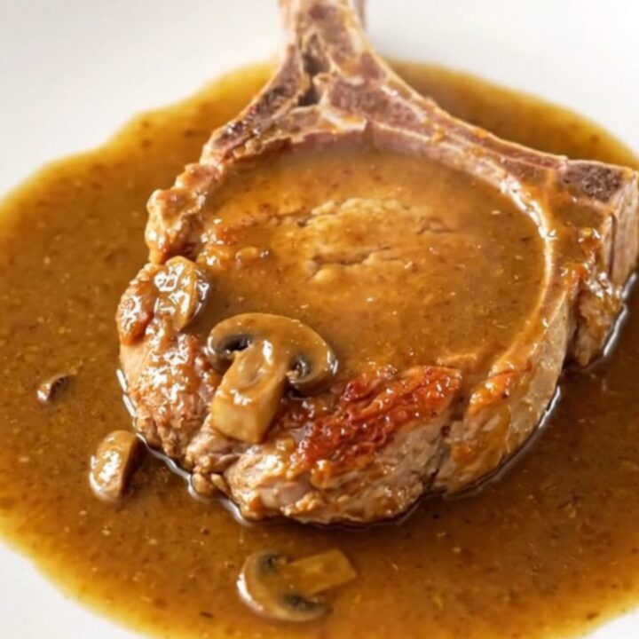 A close-up of tender, bone-in pork chops covered in a rich, creamy mushroom and onion gravy in a slow cooker.