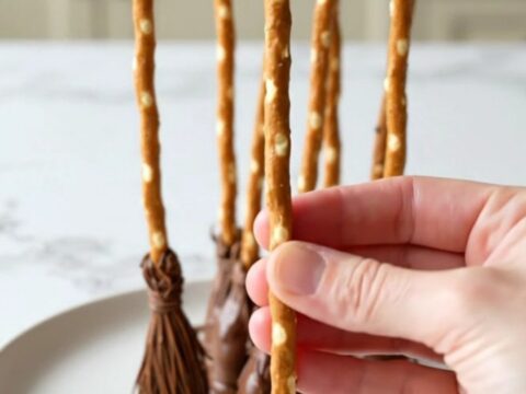 A platter filled with strawberry pretzel broomsticks with dark chocolate tips on a white plate.