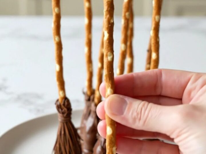 A platter filled with strawberry pretzel broomsticks with dark chocolate tips on a white plate.