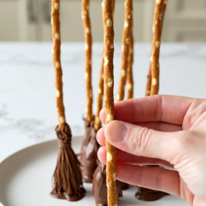 A platter filled with strawberry pretzel broomsticks with dark chocolate tips on a white plate.