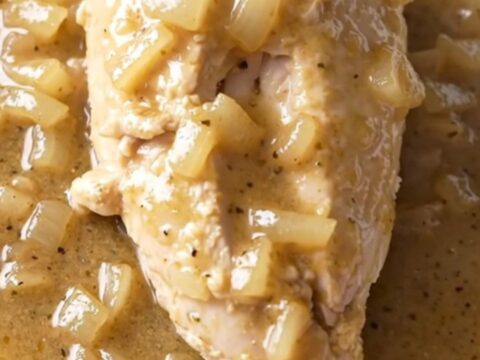 A close-up of tender chicken breasts covered in a creamy white country gravy with bits of onion.