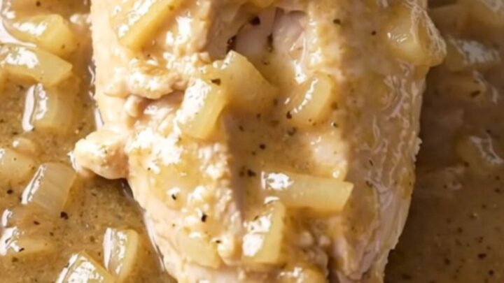 A close-up of tender chicken breasts covered in a creamy white country gravy with bits of onion.