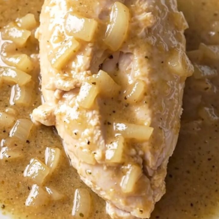 A close-up of tender chicken breasts covered in a creamy white country gravy with bits of onion.