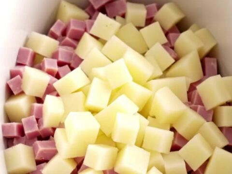 A white shallow bowl filled with creamy, loaded ham and cheddar potato soup, topped with bacon.