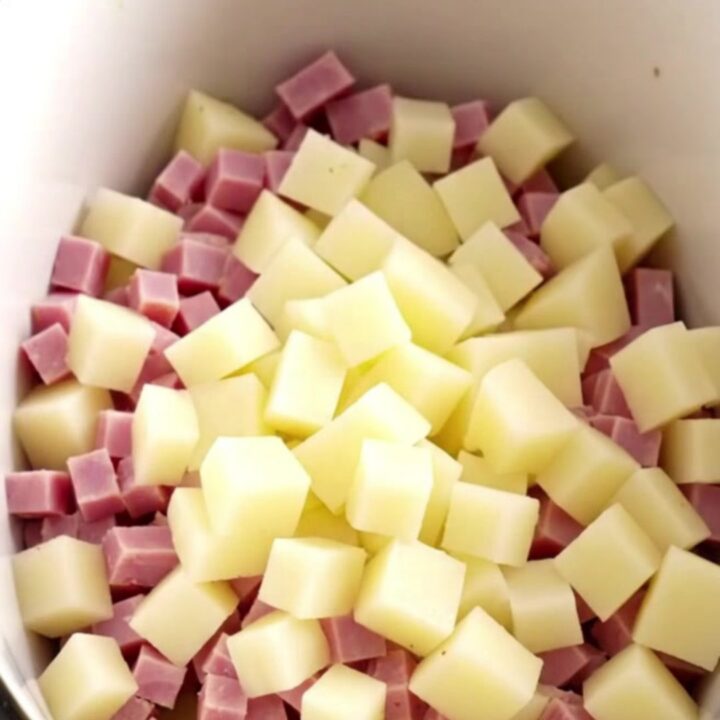 A white shallow bowl filled with creamy, loaded ham and cheddar potato soup, topped with bacon.