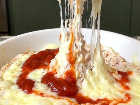 A creamy chicken parmesan dip in a slow cooker with melted cheese and red marinara sauce.