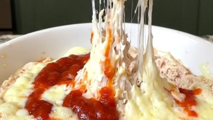 A creamy chicken parmesan dip in a slow cooker with melted cheese and red marinara sauce.
