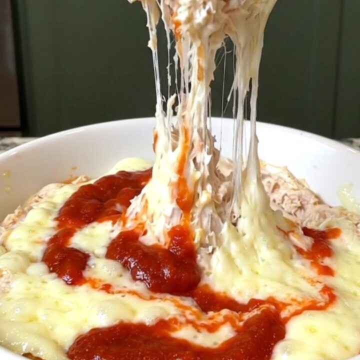 A creamy chicken parmesan dip in a slow cooker with melted cheese and red marinara sauce.