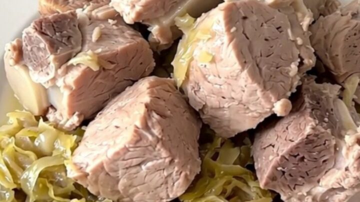 A close-up of a tender pork roast and sauerkraut served in a white bowl, showing steam rising from the dish.