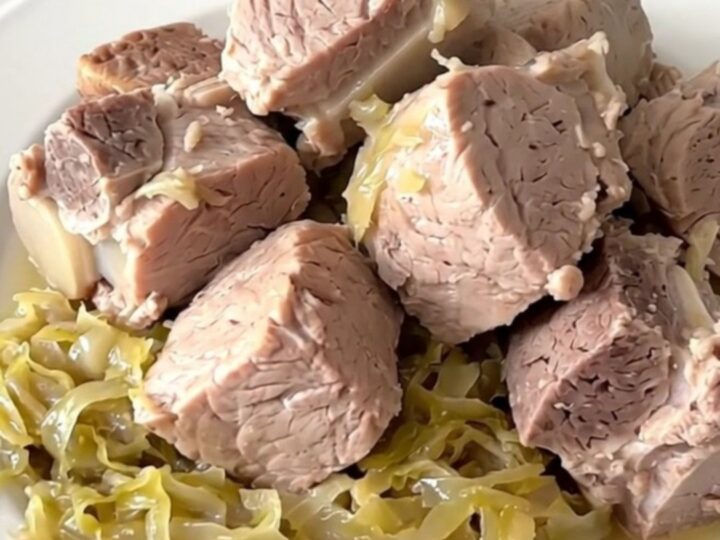 A close-up of a tender pork roast and sauerkraut served in a white bowl, showing steam rising from the dish.
