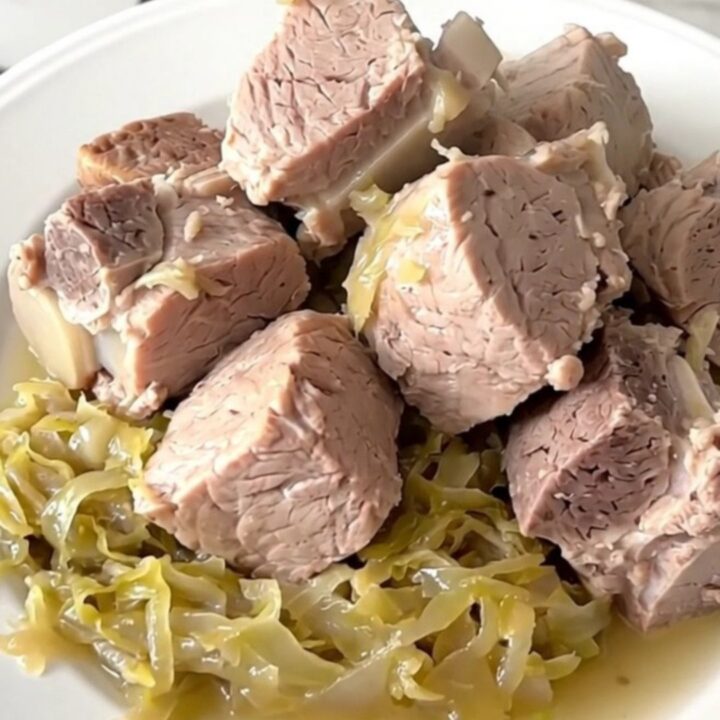 A close-up of a tender pork roast and sauerkraut served in a white bowl, showing steam rising from the dish.