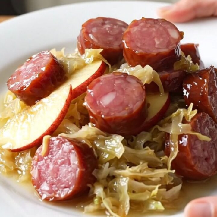 A close-up of a bowl filled with sliced kielbasa, tender sauerkraut, and soft apple wedges, steaming slightly.