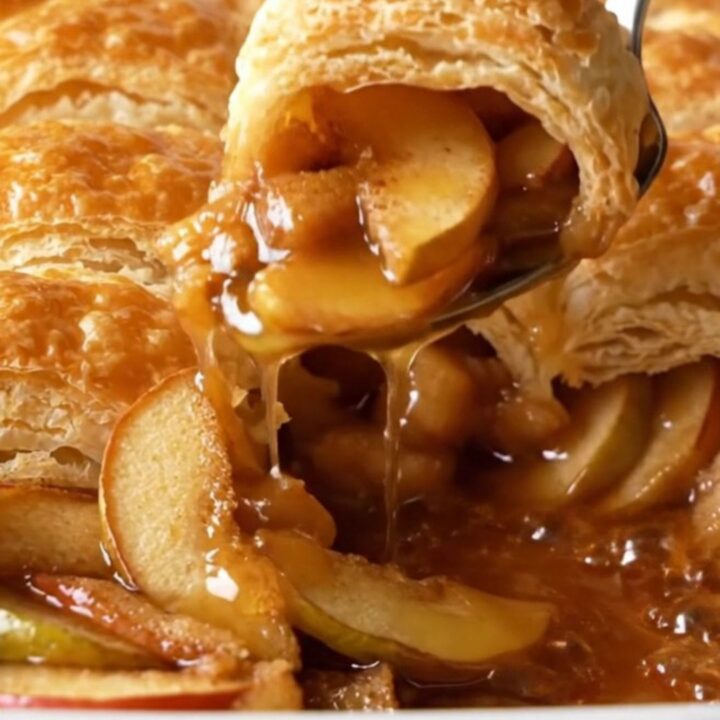 A warm puff pastry apple cobbler in a ceramic baking dish with golden crust and bubbling syrup.
