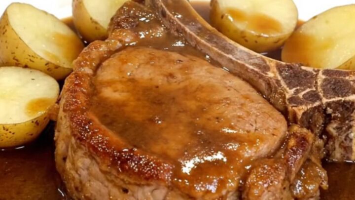 Bone-in pork chops and baby potatoes glistening in a rich brown gravy inside a slow cooker.