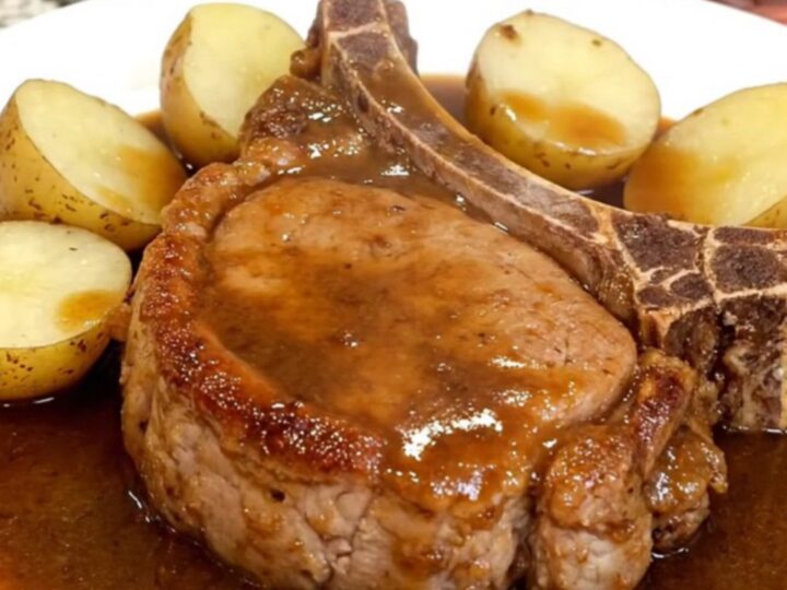 Bone-in pork chops and baby potatoes glistening in a rich brown gravy inside a slow cooker.
