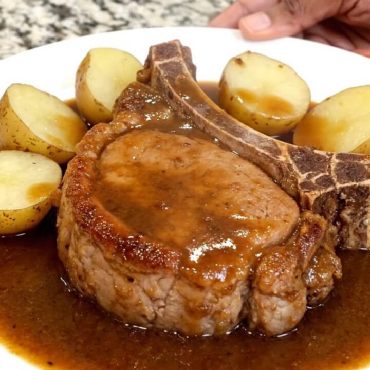 Bone-in pork chops and baby potatoes glistening in a rich brown gravy inside a slow cooker.