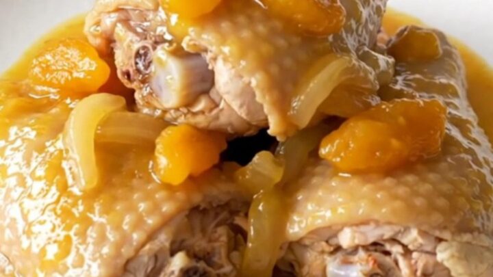 Slow cooker filled with cooked bone-in chicken thighs covered in a rich apricot and onion sauce.