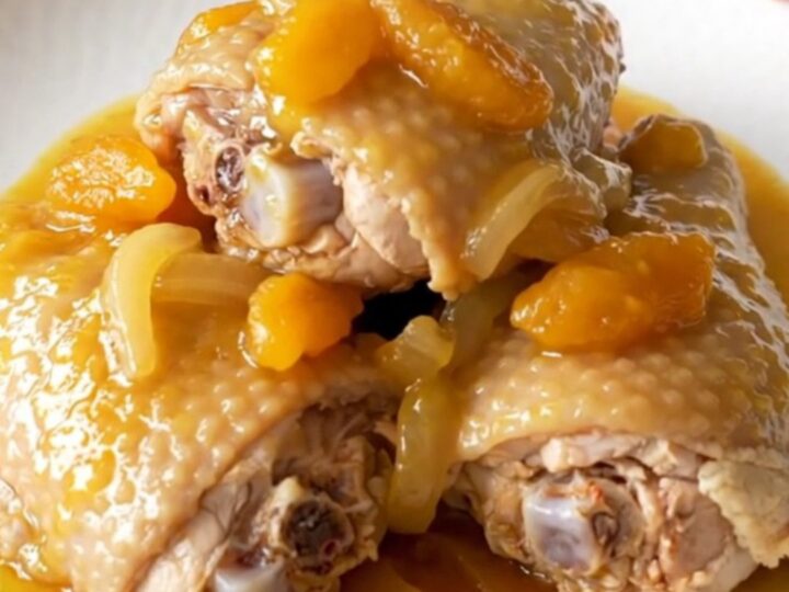 Slow cooker filled with cooked bone-in chicken thighs covered in a rich apricot and onion sauce.