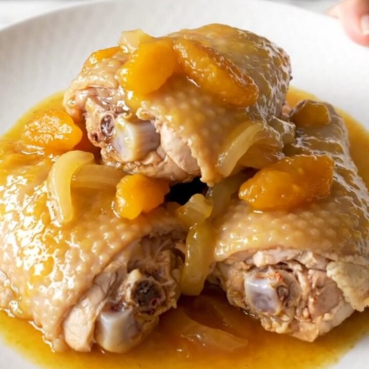 Slow cooker filled with cooked bone-in chicken thighs covered in a rich apricot and onion sauce.