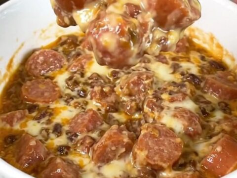A black slow cooker filled with a creamy, melted chili and cheese dip topped with hot dog slices.