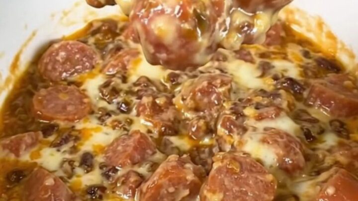 A black slow cooker filled with a creamy, melted chili and cheese dip topped with hot dog slices.